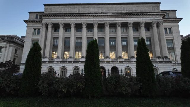 A white marble building with columns, windows, and a sign reading United States Department of Agriculture. There are bushes and trees in front of the building. The sky is blue and there is a flagpole 