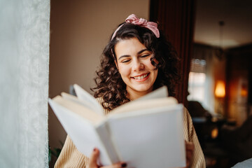 Young caucasian woman reading book or learning by the window