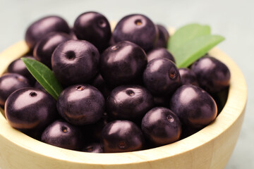 Ripe acai berries and leaves in bowl on table, closeup
