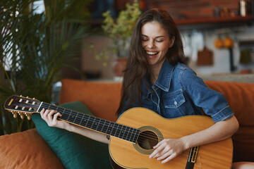 Woman playing acoustic guitar with closed eyes on a couch in a cozy living room setting