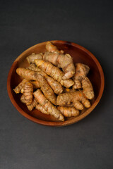 Fresh turmeric roots on wooden plate isolated on black background. High resolution photo.
