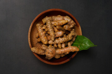 Fresh turmeric roots on wooden plate isolated on black background. High resolution photo.