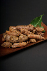 Fresh turmeric roots on wooden plate isolated on black background. High resolution photo.