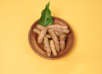 Fresh turmeric roots on wooden plate isolated on yellow background. High resolution photo.