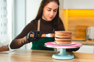 Close-up. The pastry chef covers the cake with chocolate cream using a culinary spatula.