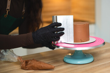 The process of a confectioner smooths the surface of a chocolate cake with a bench scraper.
