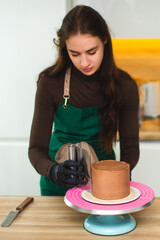 A pastry chef smooths the surface smooths the surface of a chocolate cake with a bench scraper.