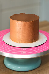 Close-up. Chocolate cake with smooth cream surface on a turntable. The process of making a chocolate holiday cake.