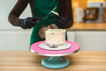 Close-up. The process of a confectioner covers the cake with white cream from a pastry bag.