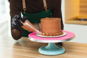 The process of a confectioner applying chocolate cream from a pastry bag onto a cake.