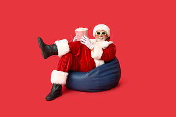 Santa Claus in 3D glasses with bucket of tasty popcorn on red background