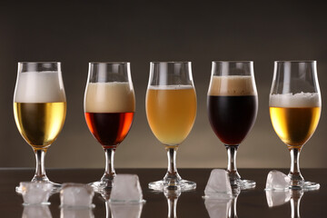 Glasses with different types of beer and ice cubes on mirror surface