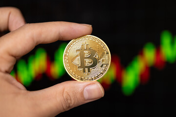 A hand holding BTC Bitcoin over a price chart