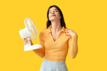 Young woman with electric fan on yellow  background