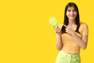 Young woman with mini fan on yellow background