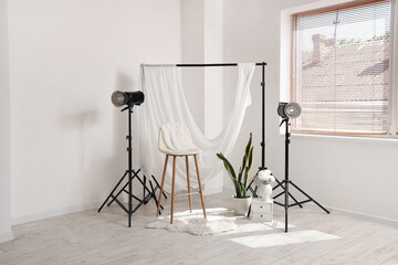 Interior of stylish photo studio with professional equipment, chair, houseplant and rug