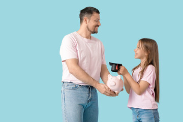 Father and his daughter holding piggy bank with mortar board on blue background. Tuition fees concept