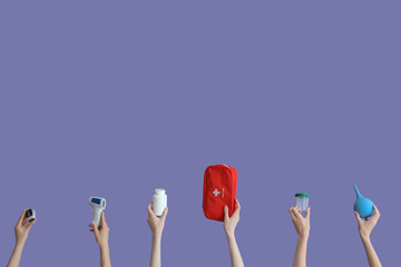 Hands with enema, first aid kit, pills, glucometer and thermometer on lilac background