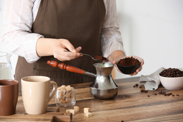 Woman filling cezve with powdered coffee on table in kitchen