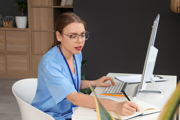 Young female medical student in eyeglasses studying with modern computer at workplace at home