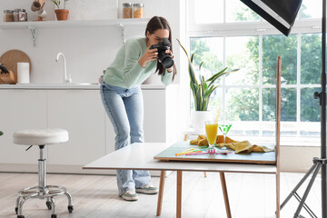 Young female food photographer with professional equipment taking top view picture of cocktails in modern kitchen