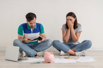 Young man looking into his empty wallet while his wife crying on floor at home. Bankruptcy concept