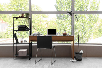 Messy workplace with laptop and papers near window in office