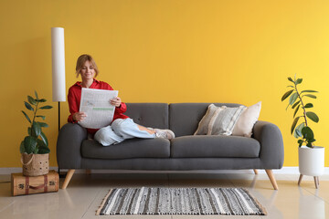 Pretty young woman reading newspaper on sofa at home