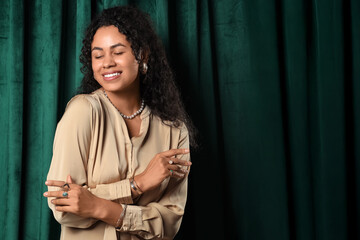 Beautiful young happy African-American woman with stylish jewellery on green fabric background