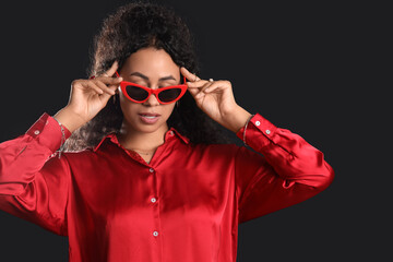 Beautiful young African-American woman in sunglasses with stylish jewellery on black background