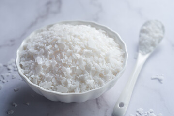 Hydrogenated castor oil wax flakes in white ceramic bowl.