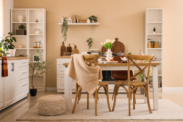 Wooden dining table, chairs, shelving units and white counters in interior of light kitchen