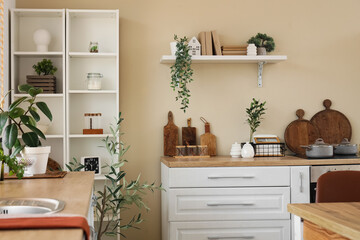 Shelving unit and white counter with utensils near beige wall in interior of light kitchen
