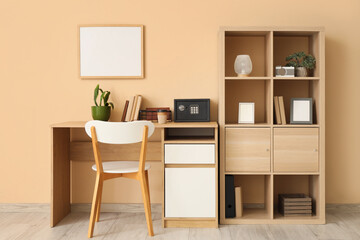 Interior of room with workplace, shelving unit and safe box on table near beige wall