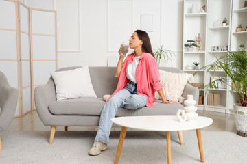 Fototapeta premium Young woman drinking chia seed water on sofa at home