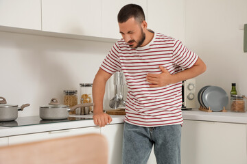 Young man having heart attack near counters in kitchen