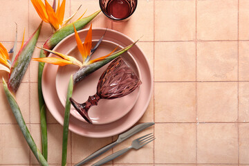 Fototapeta premium Plates with beautiful strelitzia flowers, glasses and cutlery on beige tile background