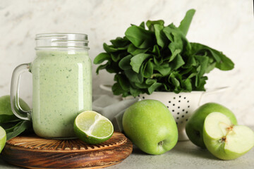 Mason jar of fresh spinach smoothie with lime and apples on white background