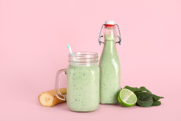 Mason jar and bottle of fresh spinach smoothie with lime and banana on pink background