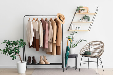 Rack with different stylish clothes and boots near armchair in living room