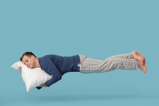 Young man flying while sleeping on blue background