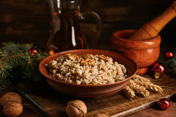 Bowl of traditional Ukrainian Kutya dish with Christmas balls and jug of uzvar on wooden background