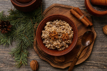 Bowl of traditional Ukrainian Kutya dish with cinnamon and Christmas tree branch on wooden background