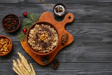 Bowl of traditional Ukrainian Kutya dish with pine cones and Christmas tree branch on black wooden background