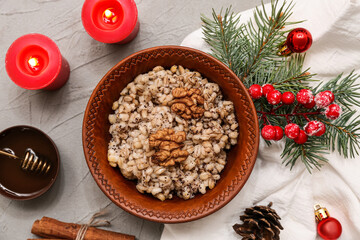 Bowl of traditional Ukrainian Kutya dish with Christmas tree branch and burning candles on grey background