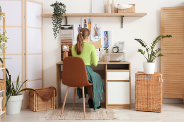 Female tailor cutting pattern at table in atelier, back view
