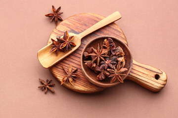 Wooden board with bowl of aromatic star anise and scoop on color background