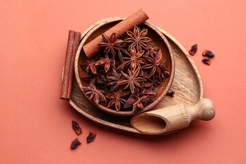 Wooden bowl with aromatic star anise and cinnamon sticks on color background