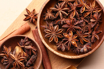 Wooden board with bowls of aromatic star anise and cinnamon on color background, closeup