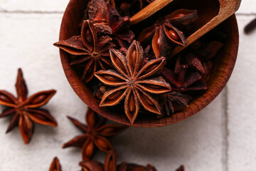 Wooden bowl with aromatic star anise and scoop on light tile background, closeup